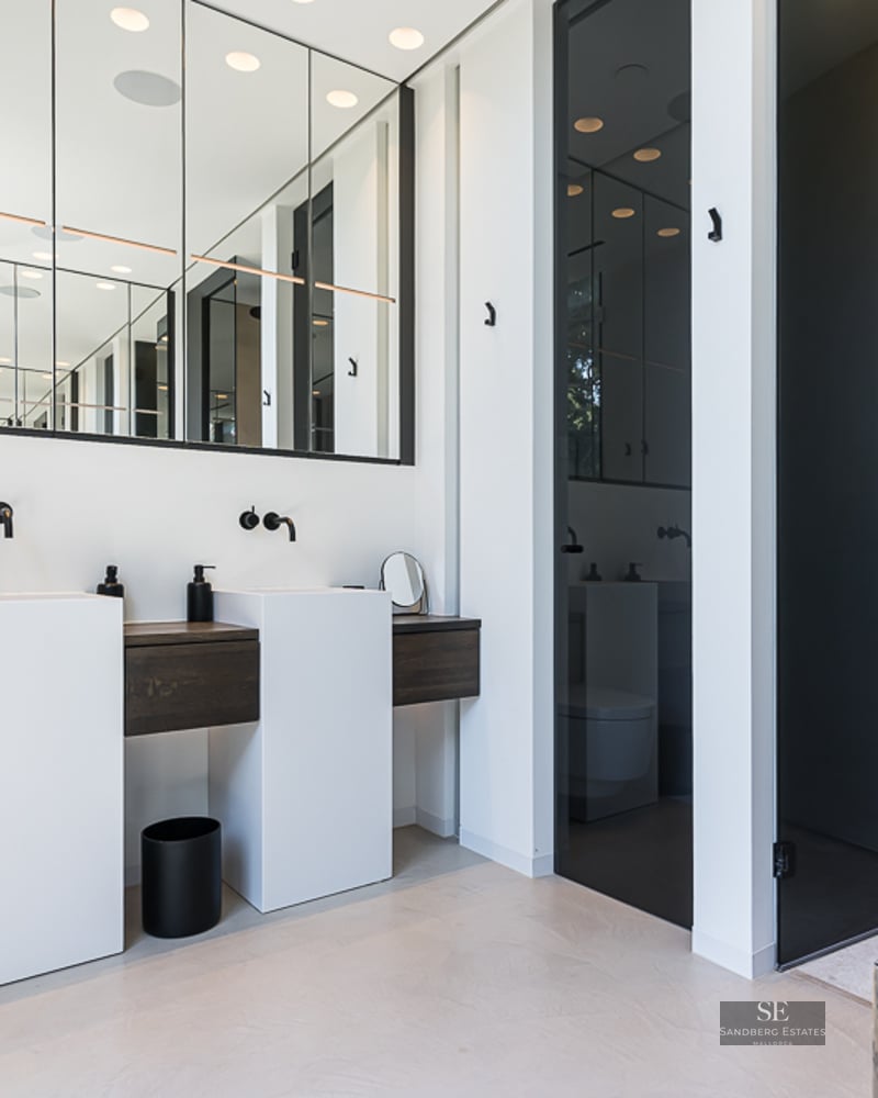 Modern bathroom featuring two white pedestal sinks, dark wood accents, and a large wall mirror.