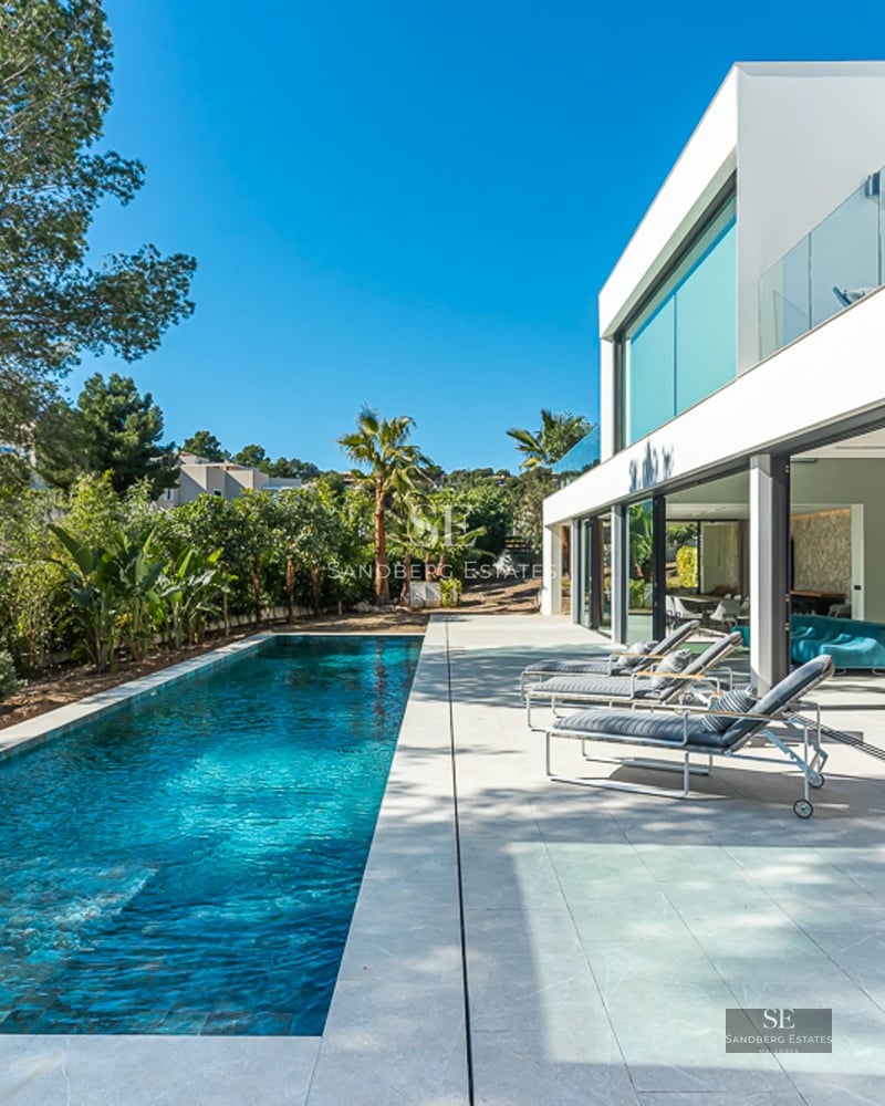 Vue d'une piscine moderne avec des chaises longues et des parasols. Architecture épurée et minimaliste, entourée de verdure.