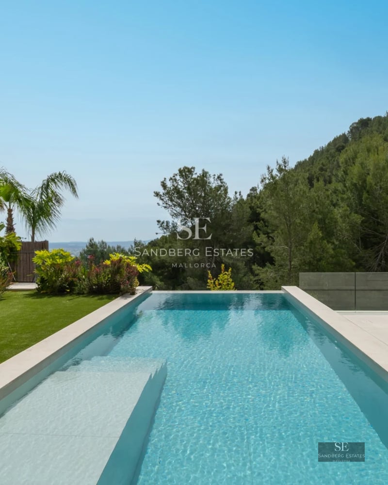 Exterior view of a modern villa featuring a reflective pool, expansive windows, and minimalist design in a landscaped setting.
