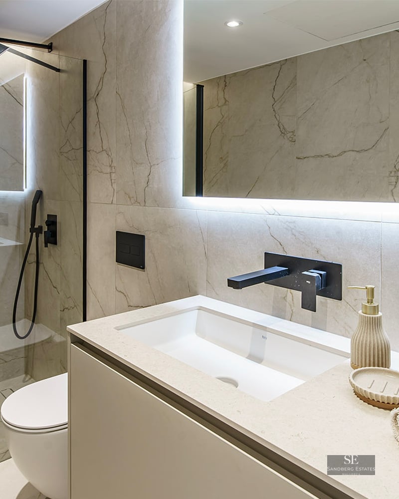 Contemporary bathroom featuring a glass walk-in shower, black fixtures, marble-effect tiles, and a backlit mirror.