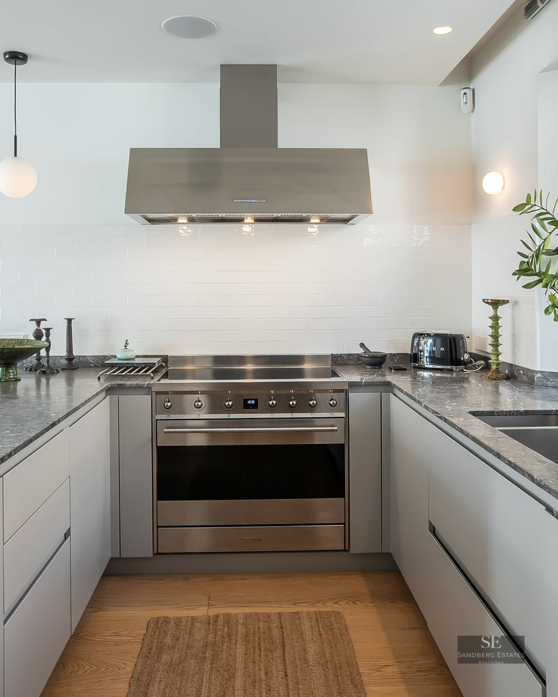 Modern U-shaped kitchen with grey stone countertops, stainless steel appliances, and natural light from a window.