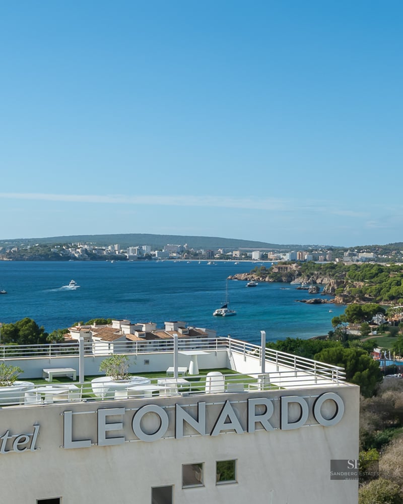 Panoramic view of a Mediterranean bay and coastline from a modern rooftop terrace with white railings and artificial turf.