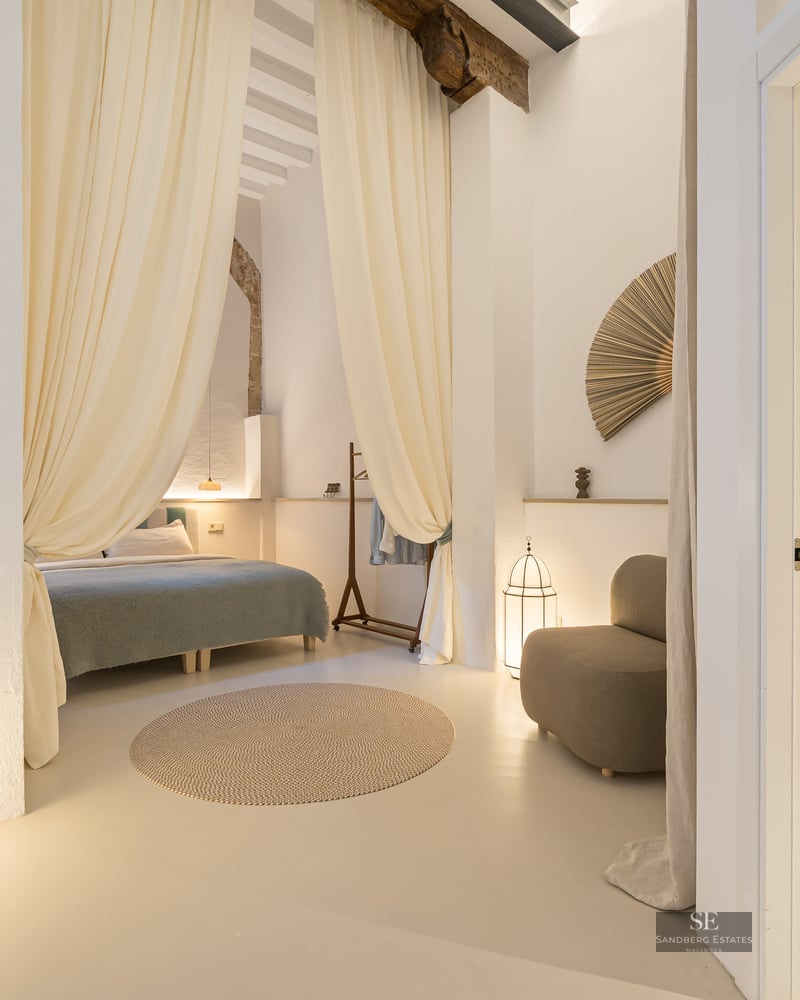 Chambre principale avec rideaux en lin, salle de bain attenante avec vasque en pierre, poutres et éclairage chaleureux.