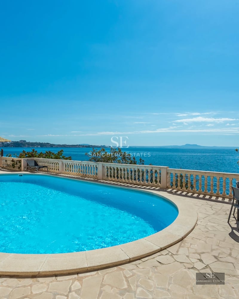 Oval swimming pool on a stone terrace overlooking the Mediterranean Sea under a clear blue sky.