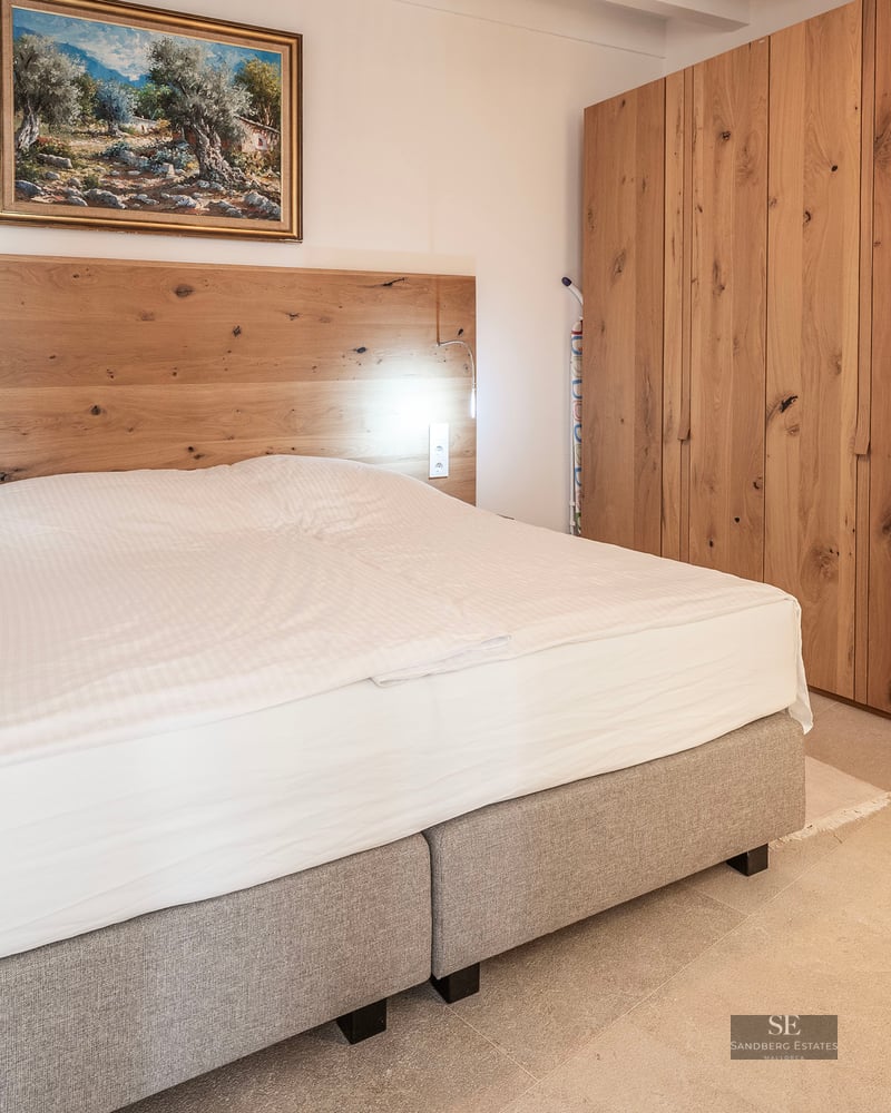 Chambre moderne avec un grand lit, une tête de lit en bois, de grandes armoires en chêne et un tableau au mur.