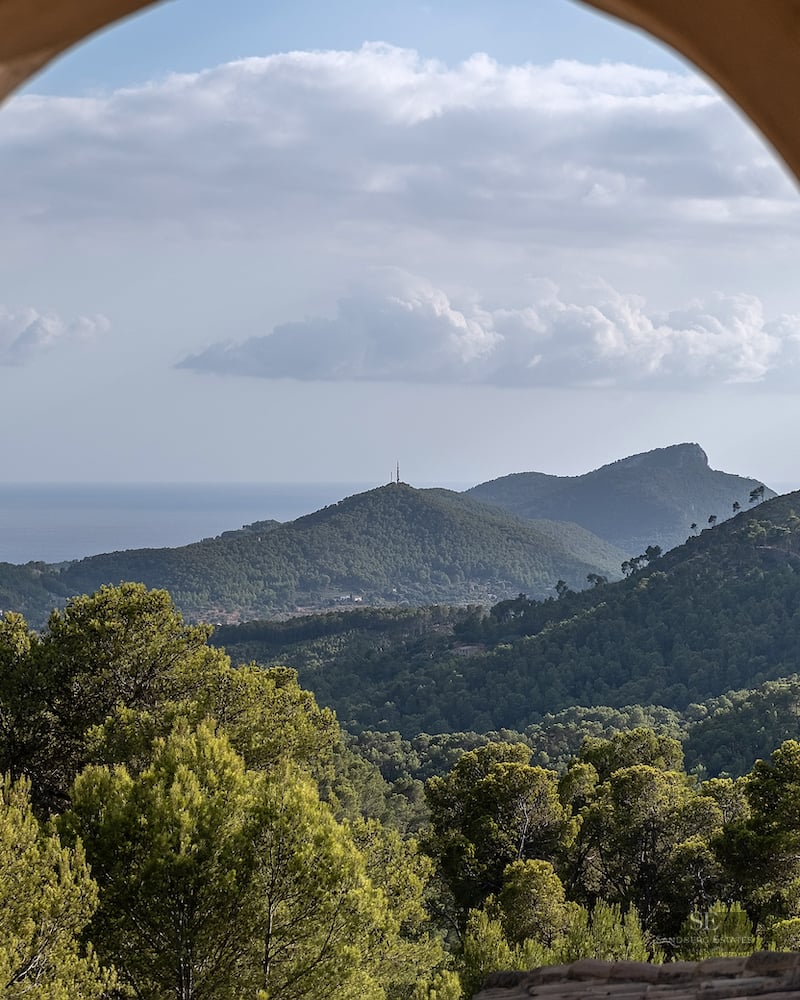 A view of lush green mountains and the distant sea framed by a traditional stone archway.