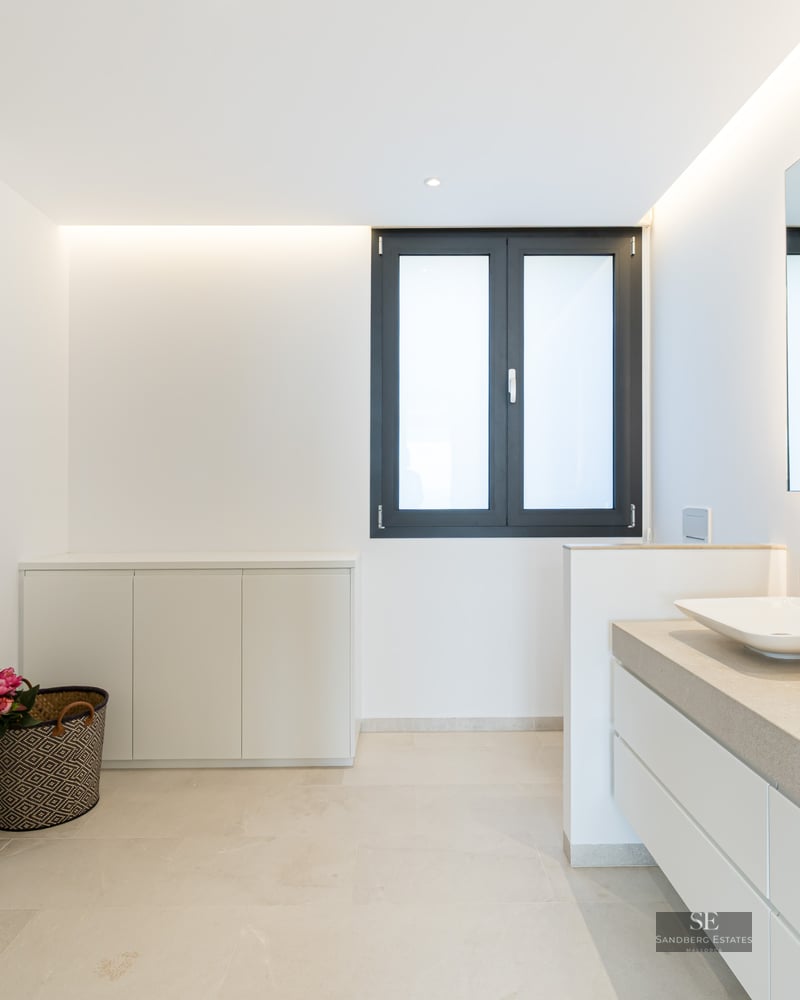 Modern master bathroom with a walk-in glass shower, double vessel sinks on stone counters, and a large backlit mirror.