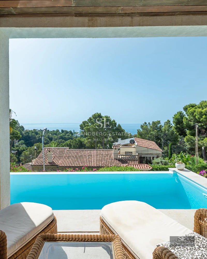 View of a modern villa with an infinity pool, terrace with sun loungers, and lush vegetation. Elegant and bright architecture.