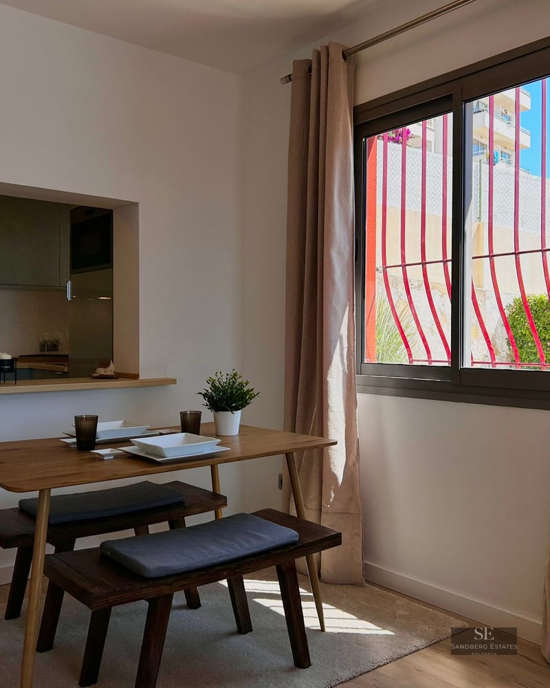 Minimalist dining room with a wooden table, benches, and a window view of red decorative bars.