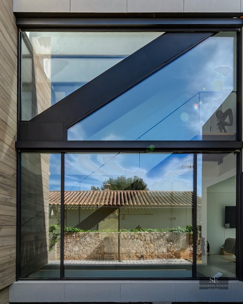 Minimalist facade featuring large glass windows, black frames, and stone and wood cladding.