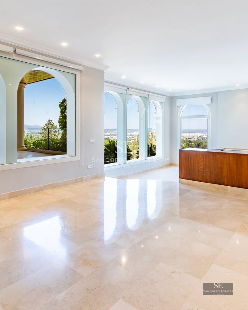 Spacious living room with fireplace, large windows, and minimalist decor. Designer pendant lamp. Light wood floors and neutral rug.