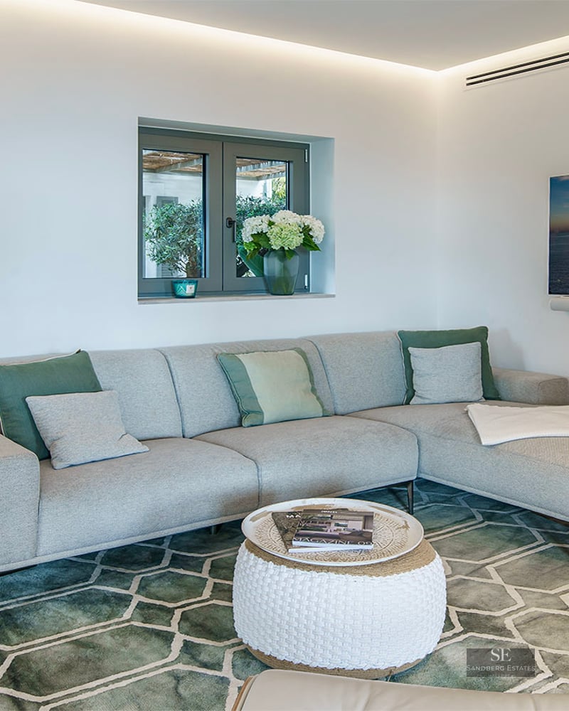 Interior view of a contemporary living room featuring a grey sectional sofa, green geometric rug, and wall-mounted TV.
