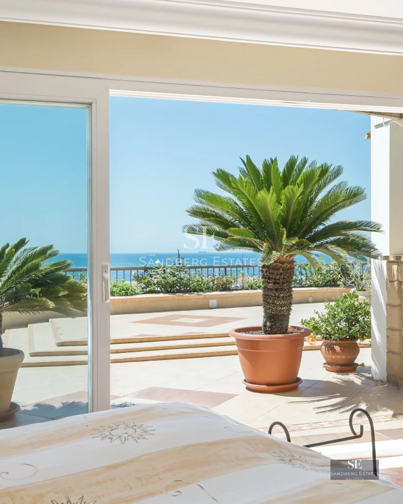 Pool view featuring sun loungers, palm trees, and modern facade. Large windows, warm lighting, and minimalist design.
