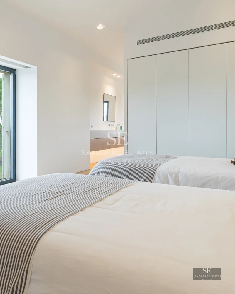 Exterior view of a luxurious villa with an infinity pool, manicured garden, and modern architecture featuring large windows.