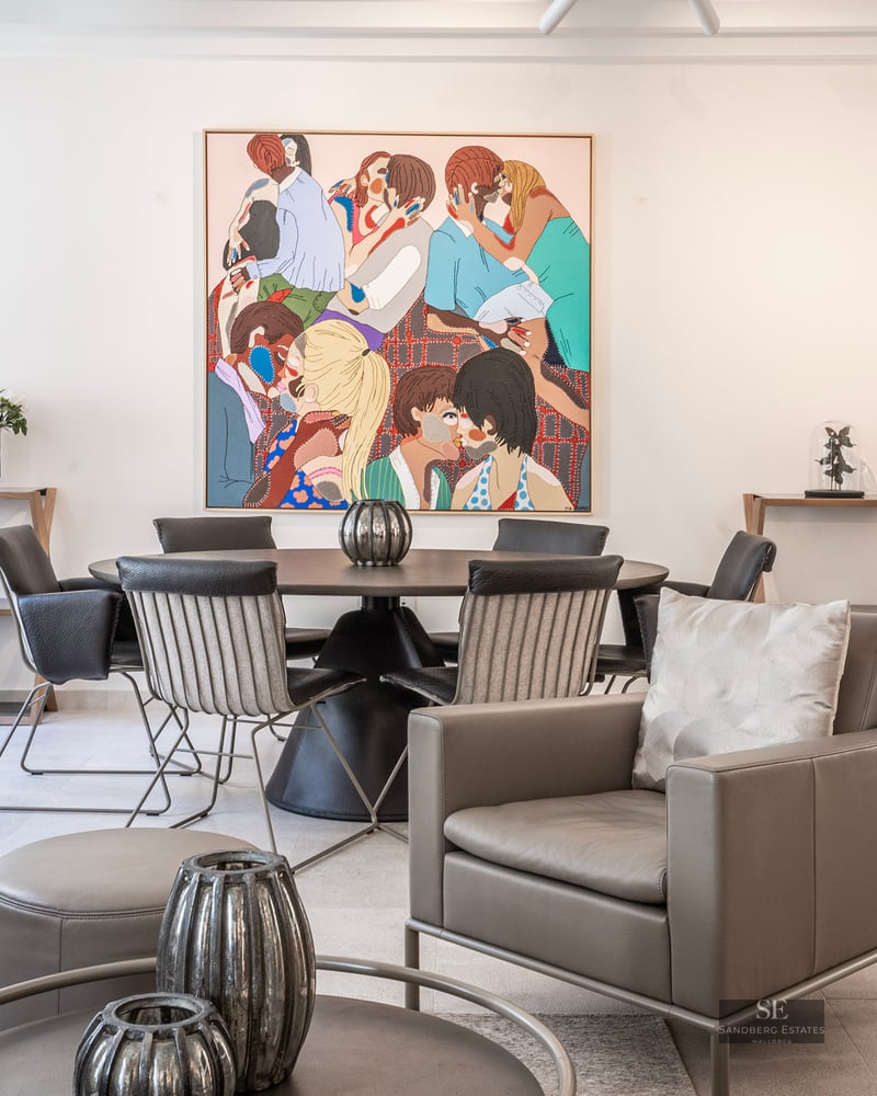 Pièce moderne lumineuse avec un fauteuil en cuir gris, une table à manger ronde et un grand tableau coloré au mur.