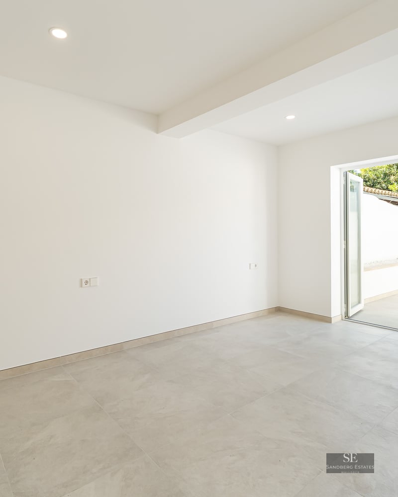 Bright, empty modern room with light gray tile floor, white walls, built-in wooden closet, and glass door to a patio.