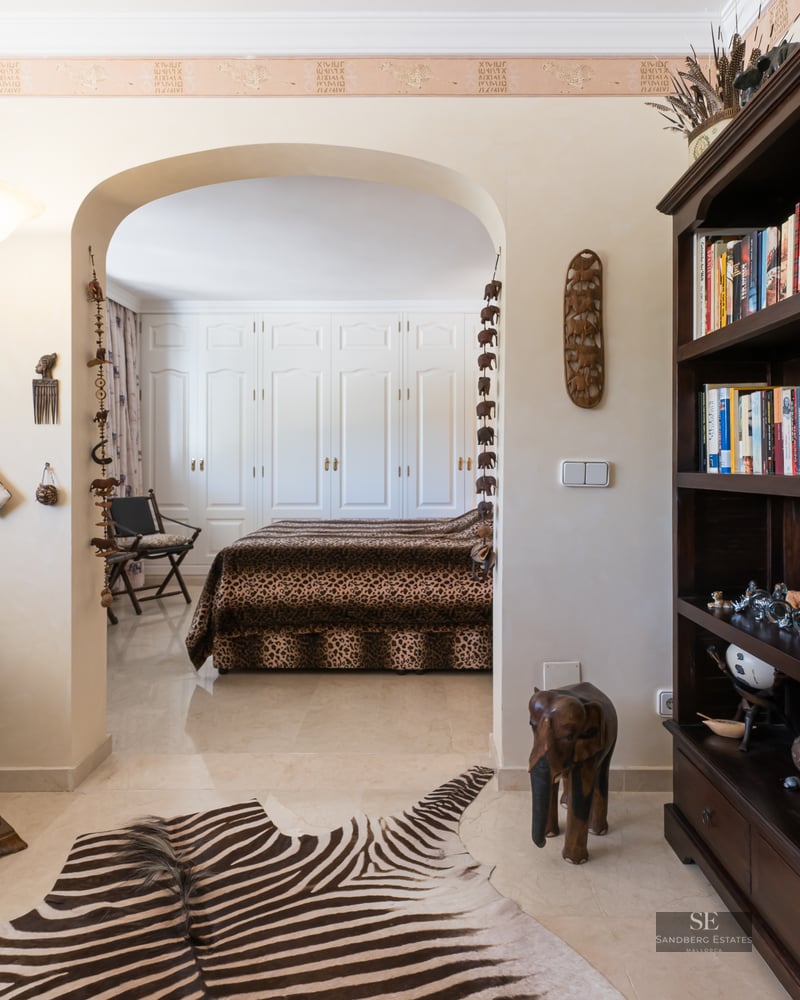 African-themed sitting room with zebra rug and chair leading through an archway to a bedroom with leopard print bedding.