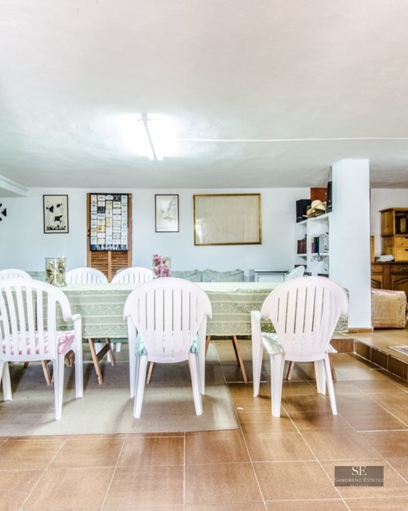 Large dining table with white chairs in a tiled room with traditional decor and floral curtains.