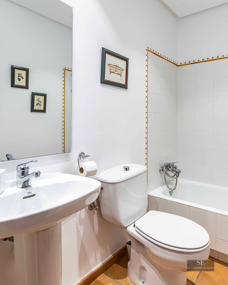 Bathroom with white wall tiles, bathtub, pedestal sink, toilet, and terracotta floor tiles.