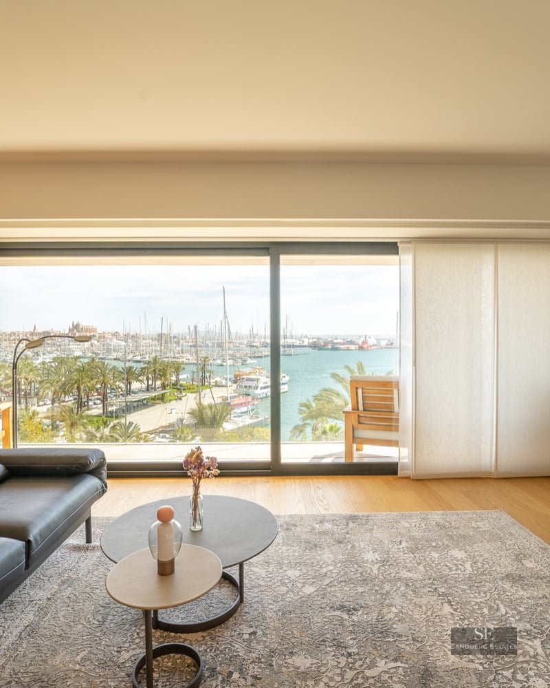 Modern living room featuring a black leather sofa and large glass sliding doors overlooking a harbor with many boats.