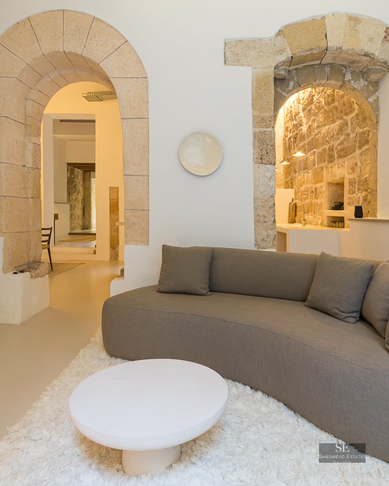Minimalist living room featuring a curved grey sofa, white shaggy rug, and historic stone archways.