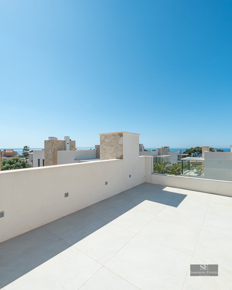 Wide white-tiled rooftop terrace with a low wall and glass railing, overlooking modern villas and the ocean.