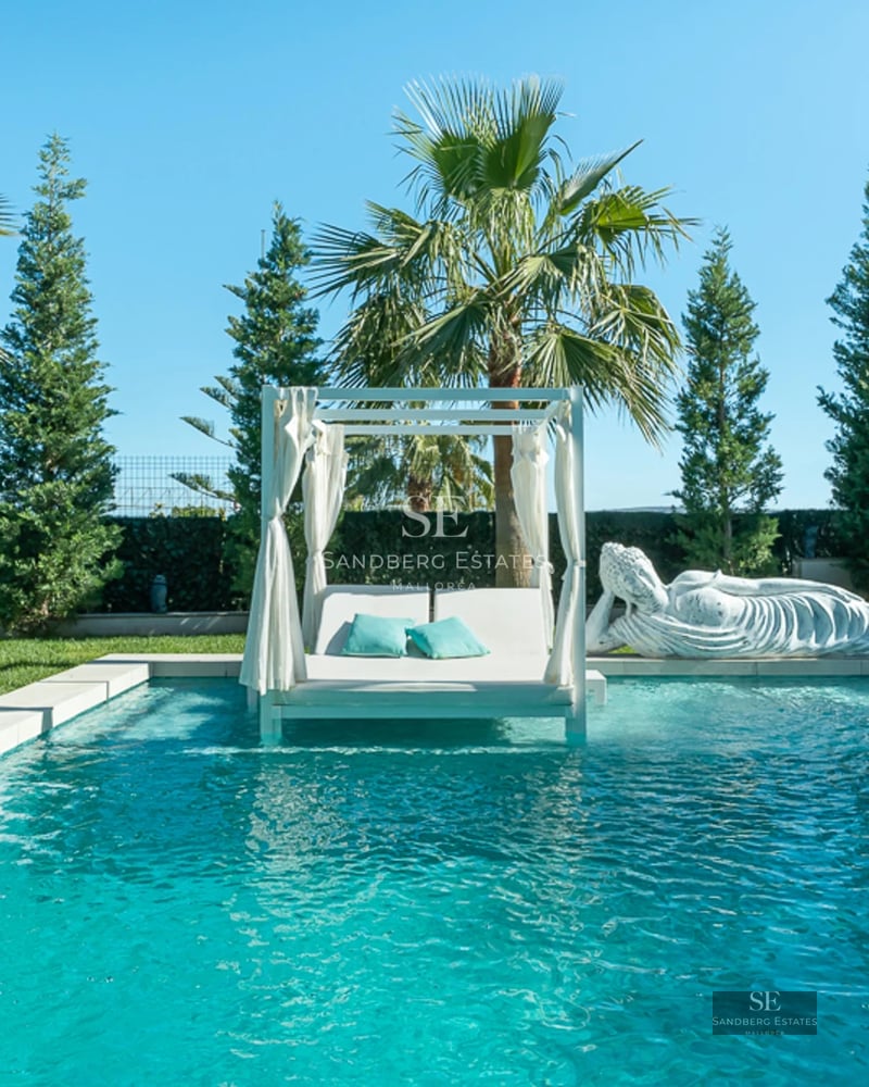 View of infinity pool with lounge chairs, surrounded by lush garden. Modern architecture with large windows and balcony.