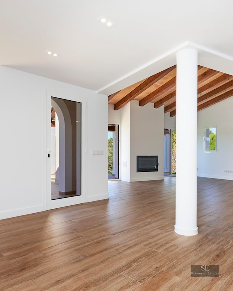 Open-plan living room with wood-look tile flooring, exposed beams, a white fireplace, and direct garden access.
