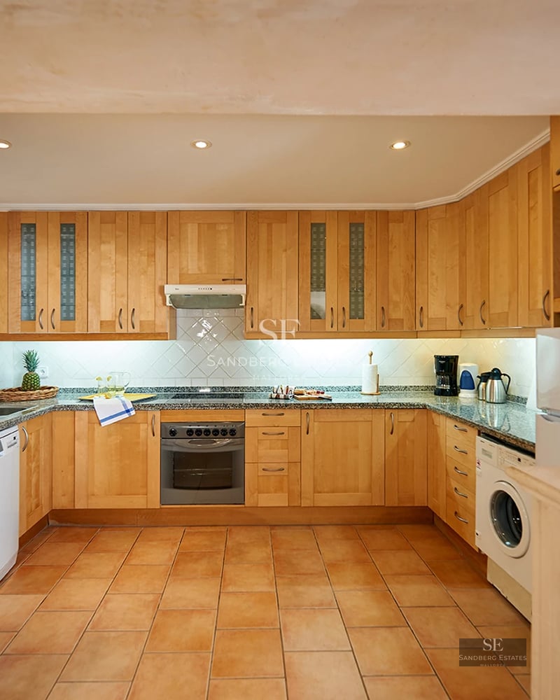 View of an elegant pool with sun loungers and umbrellas, surrounded by lush greenery and a modern house.