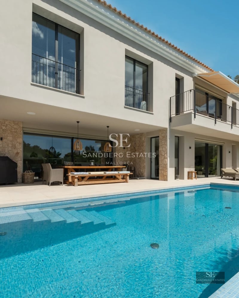 View of turquoise pool, lush garden, modern architecture, white facade, large windows, light reflections, blue sky.