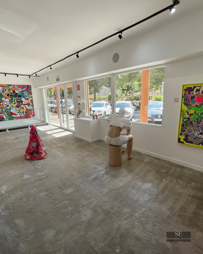 A modern art gallery with concrete floors, white walls, vibrant contemporary paintings, and a sitting sculpture.