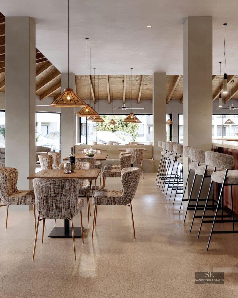 Modern bar with wooden beamed ceiling, wicker pendant lights, and upholstered bar stools.