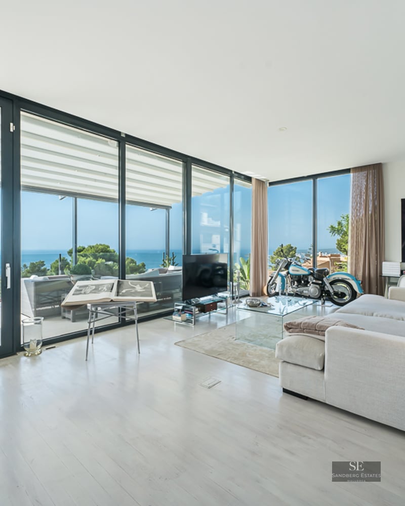 Bright, spacious living room with floor-to-ceiling glass doors, a large white sofa, and a breathtaking view of the ocean.