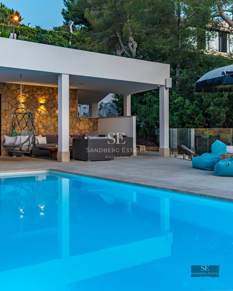 Spacious living room with floor-to-ceiling windows, light wood floors, beige sofas, wool rug, fireplace, and panoramic sea views. Modern and bright design.