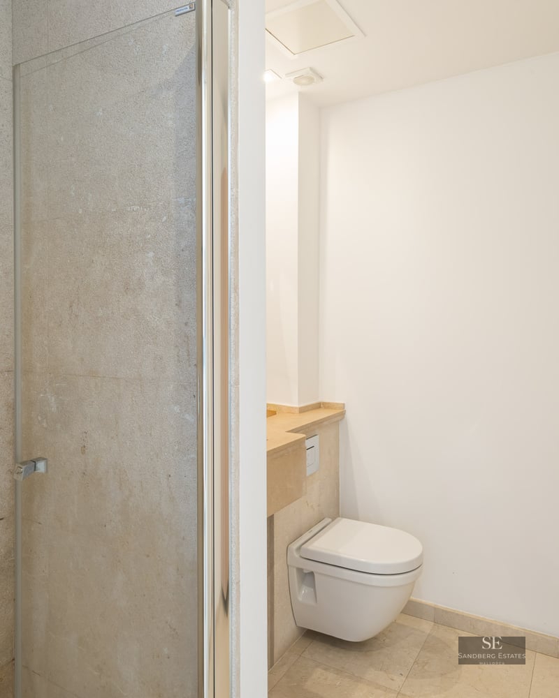 Bathroom featuring a glass walk-in shower, wall-mounted toilet, and beige stone walls.