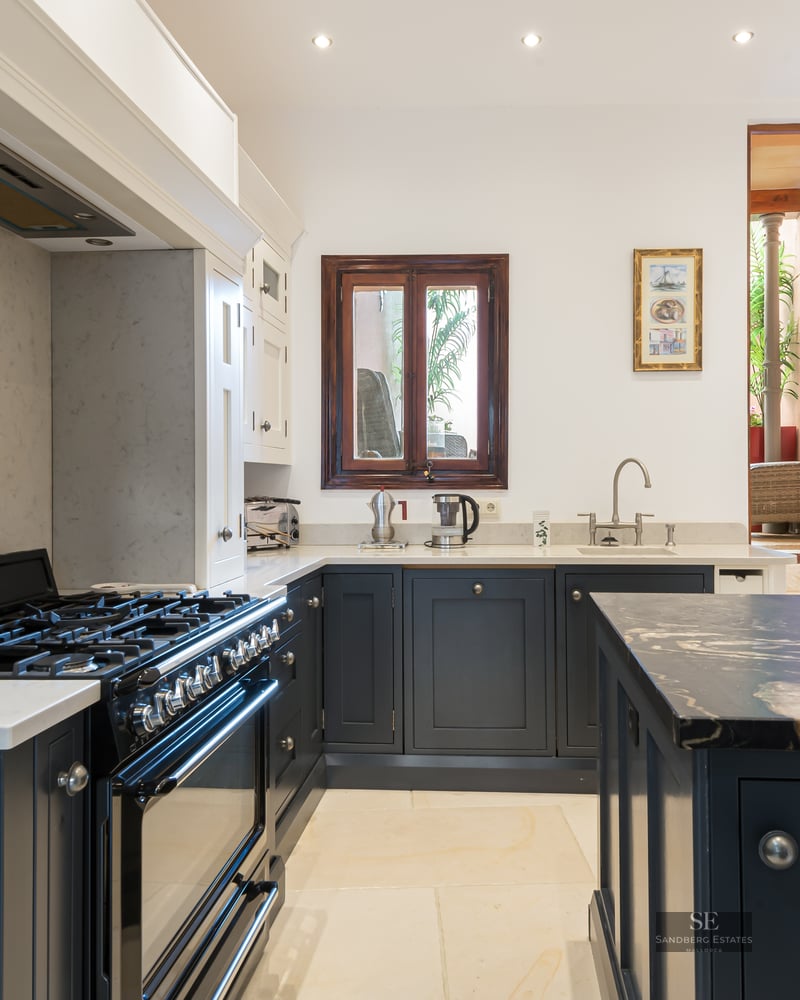 Kitchen with navy blue cabinets, white marble countertops, a Smeg range stove, and a natural stone feature wall.