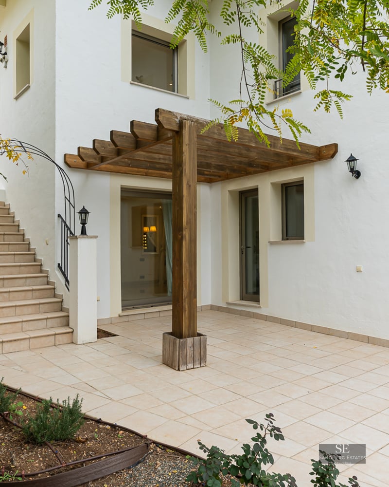 White building exterior with a tiled patio, wooden pergola, and stone stairs leading to an upper level.
