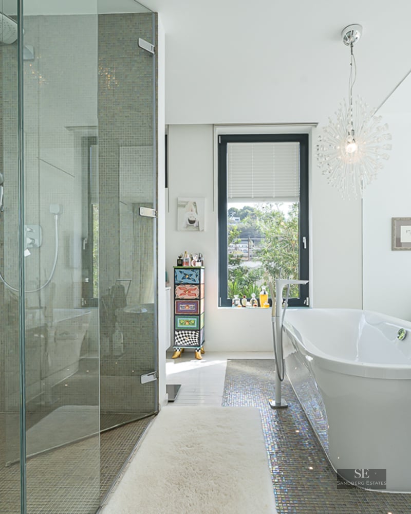 Modern master bathroom featuring a glass walk-in shower and a sleek freestanding bathtub with mosaic tile flooring.