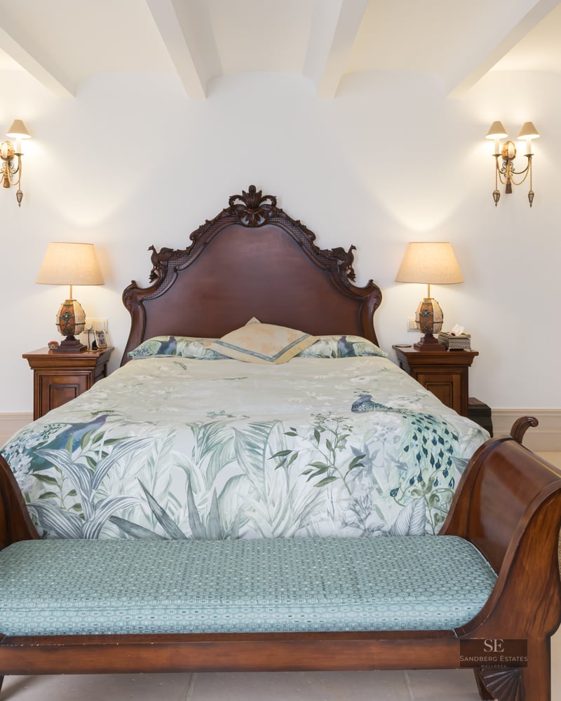 Bedroom featuring a large carved wood headboard, floral bedding, matching nightstands, and built-in white wardrobes.