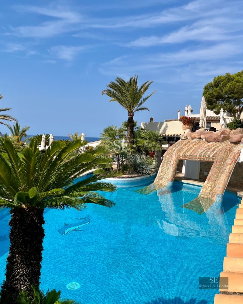 View of infinity pool, garden with lawn, outdoor seating area. Modern architecture with large windows and landscaping.