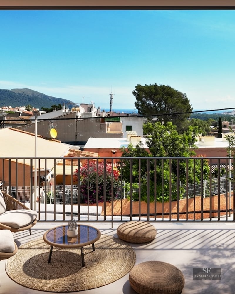 Sun-drenched terrace with wicker armchairs, olive trees, and views of a Mediterranean town and mountains.