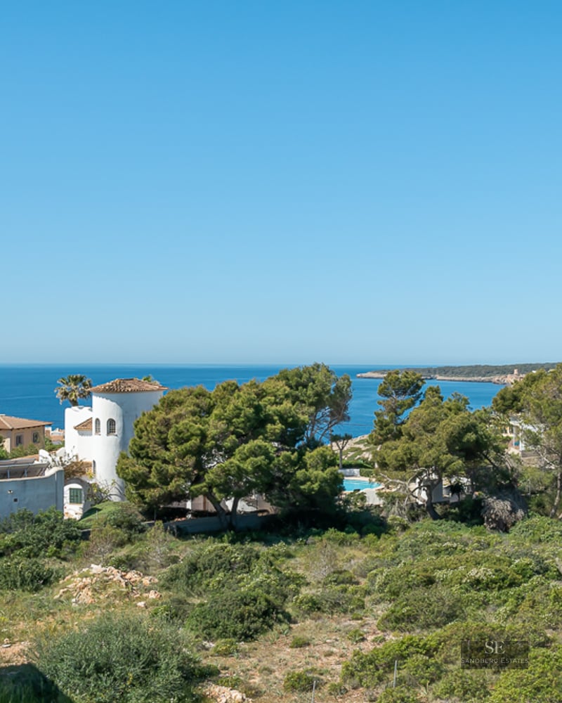 High-angle view of the blue Mediterranean sea behind lush green trees and white Mediterranean villas.