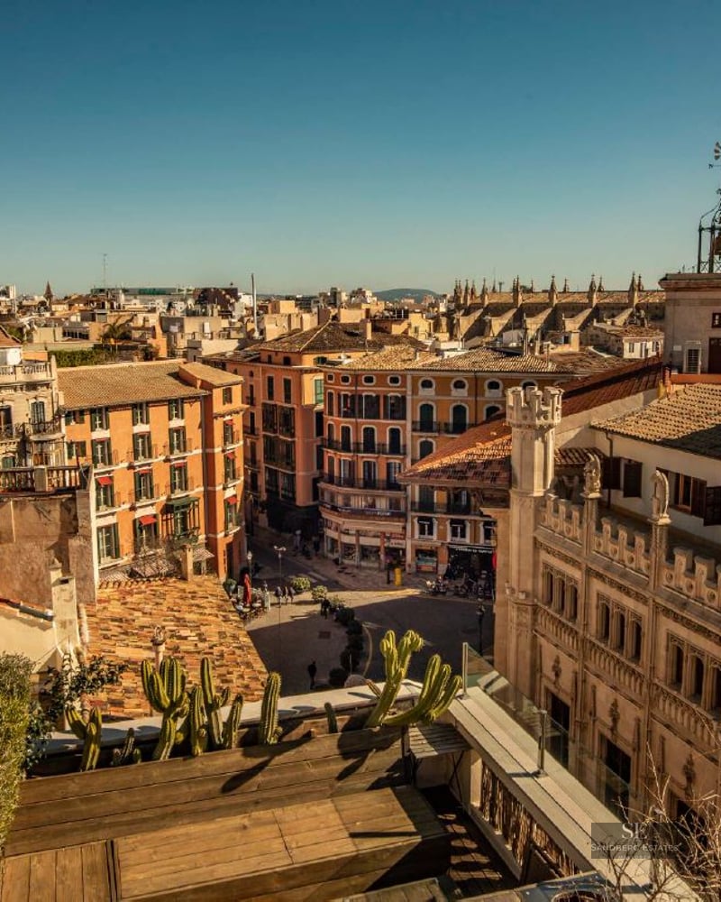 High-angle view of Mediterranean city rooftops and a Gothic cathedral spire under a bright blue sky.