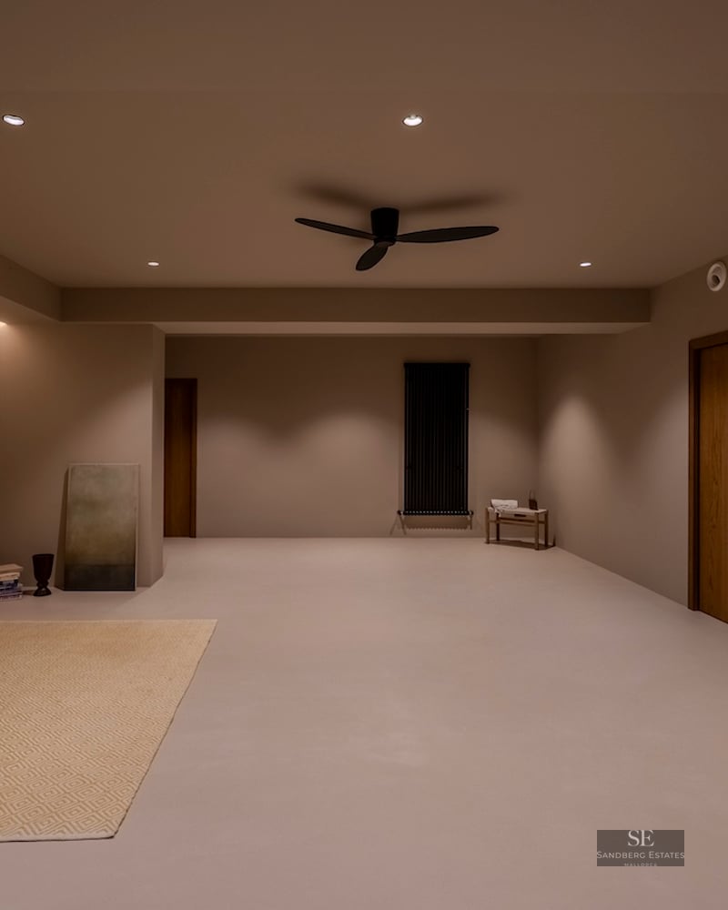 Une grande pièce minimaliste avec un éclairage chaleureux, des murs taupe, des portes en bois et un ventilateur noir.