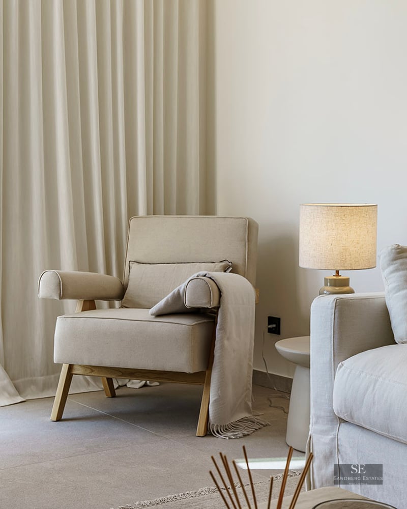 Bright living room corner featuring a cream sofa, armchair, bouclé chair, and soft floor-to-ceiling drapes.