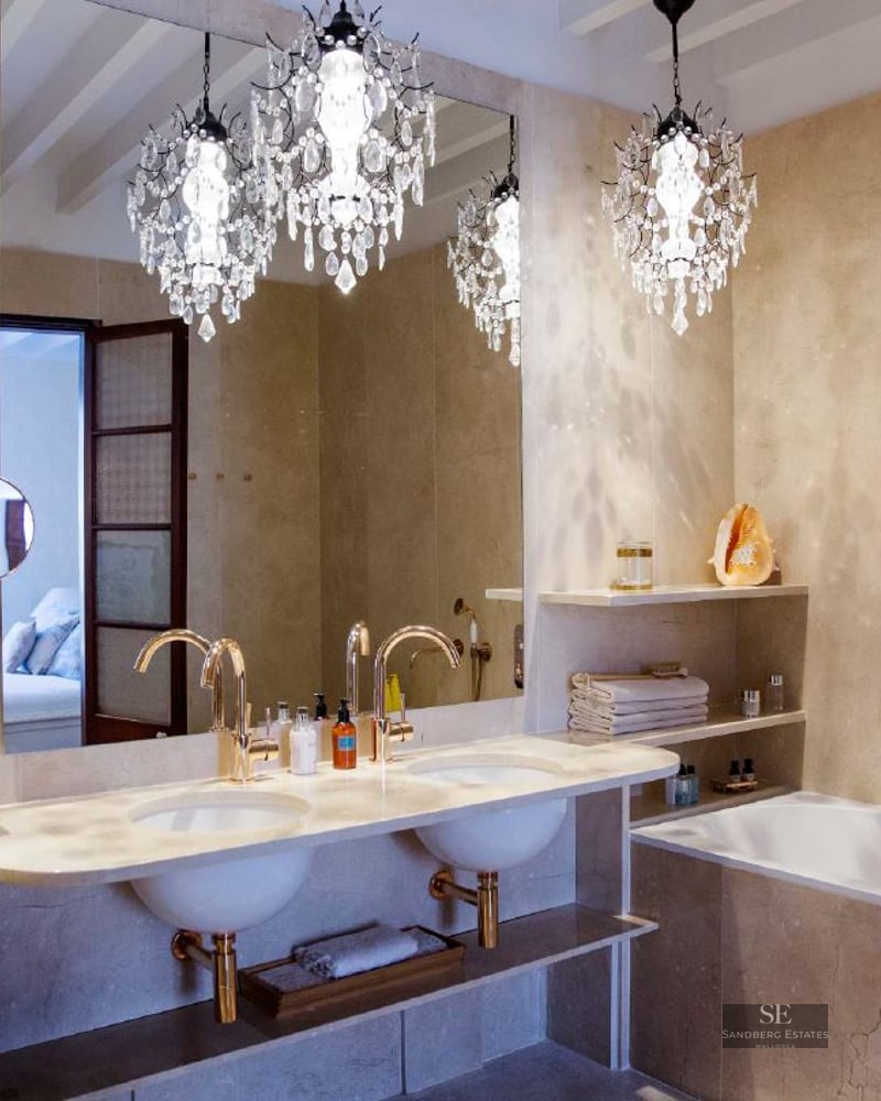 Luxurious bathroom featuring a double vanity, gold fixtures, marble walls, and three ornate crystal chandeliers.