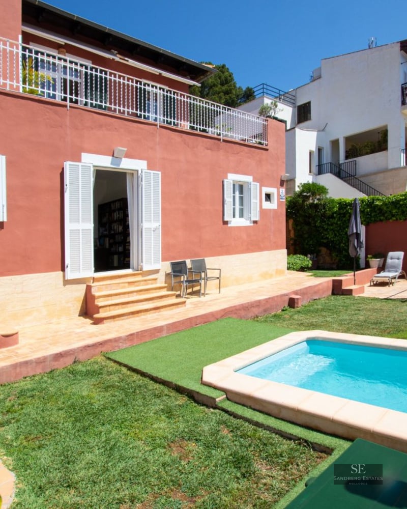 Terracotta-colored villa with a bright blue pool, lawn, and white shutters under a clear sky.