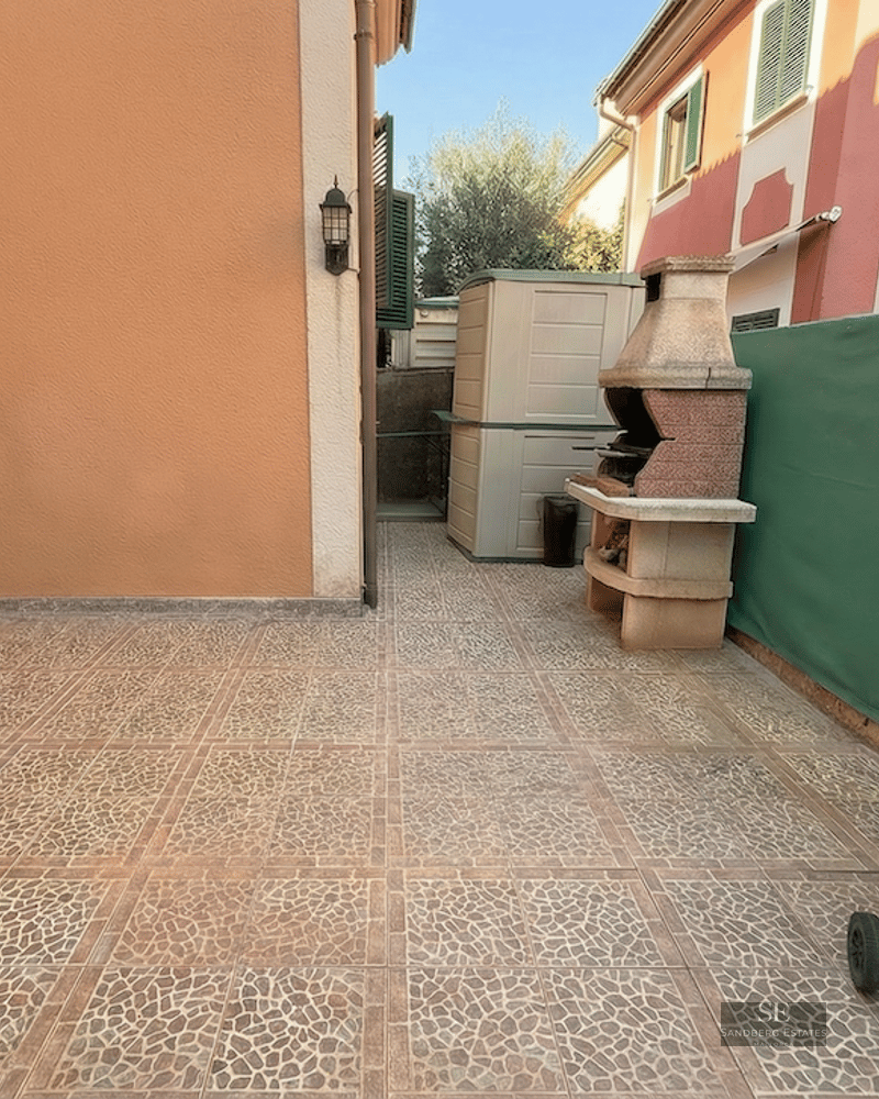 Outdoor patio with stone-patterned tiles, a masonry BBQ, a portable kettle grill, and a green privacy screen.