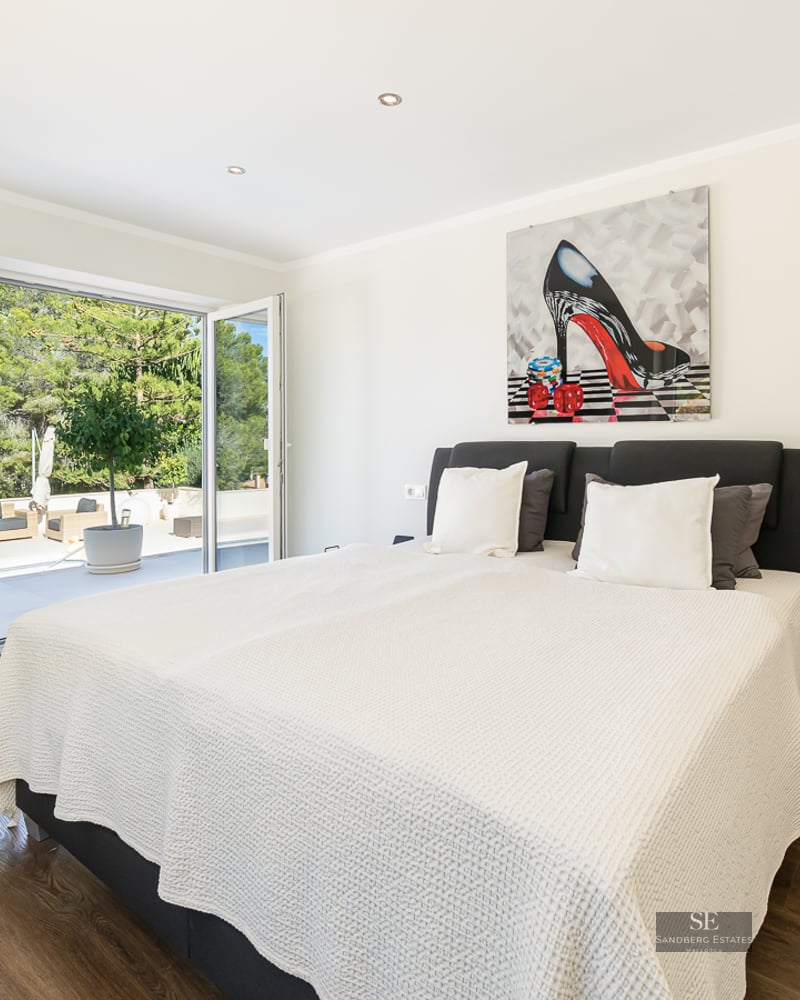 Chambre lumineuse avec grand lit, parquet foncé et portes vitrées pliantes ouvrant sur une terrasse ensoleillée.