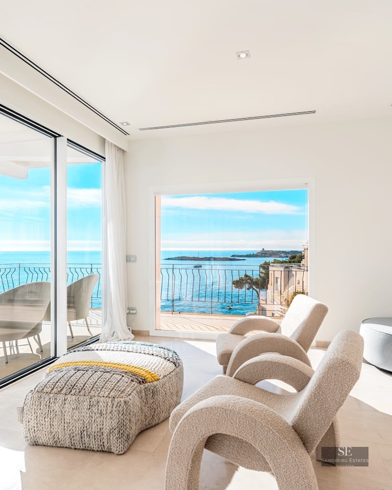 Modern white living room with designer chairs and large windows overlooking the Mediterranean sea and a terrace.